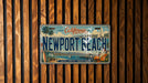 A vintage California license plate with the text "Newport Beach" is displayed on a wooden wall.