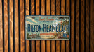 A vintage license plate with a tropical beach theme, mounted on a wooden wall.