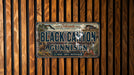 A metal sign with the text "Black Canyon of the Gunnison" is displayed against a wooden background.