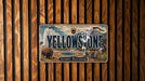 A license plate with the text "Yellowstone" and an illustration of a buffalo and a geyser, mounted on a wooden wall.