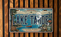 A vintage-style license plate from Lake Tahoe, California, Nevada, featuring a scenic mountain landscape with a lake, boat, and ski lift.