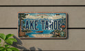 A vintage license plate from Lake Tahoe, Nevada, featuring a scenic landscape with mountains, a lake, and a boat.