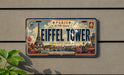 A vintage-style license plate with the text "PARIS Le Ville Lumiere Eiffel Tower Depuis 1889" and various decorative elements, including the Eiffel Tower and other Parisian landmarks.
