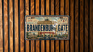 A vintage-style license plate with the text "Brandenburg Gate" displayed prominently, mounted on a wooden wall.