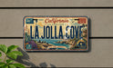 A vintage California license plate with the text "LA Jolla Cove" and a coastal theme, mounted on a wall.